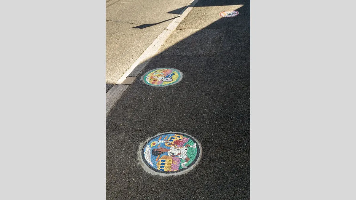 Two colourful tiled mosaics embedded in a footpath cast in shadow
