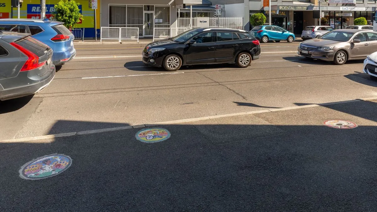 A footpath in shadow with 3 round, tiled mosaics embedded in it