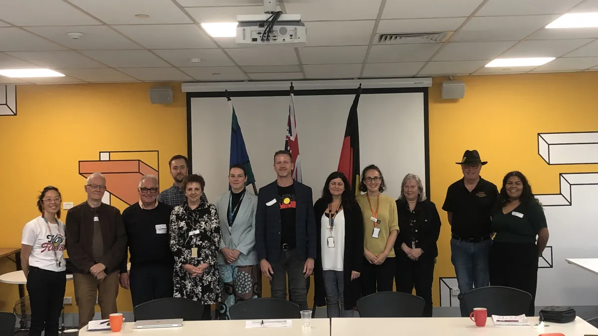 group of 12 people standing together in a meeting room in front of the Australian, Aboriginal, and Torres Strait Island flags