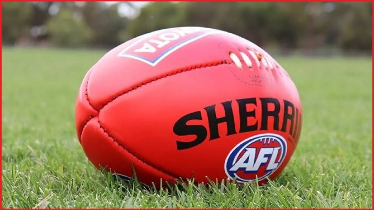 A red football with logos lies on a grassy field.