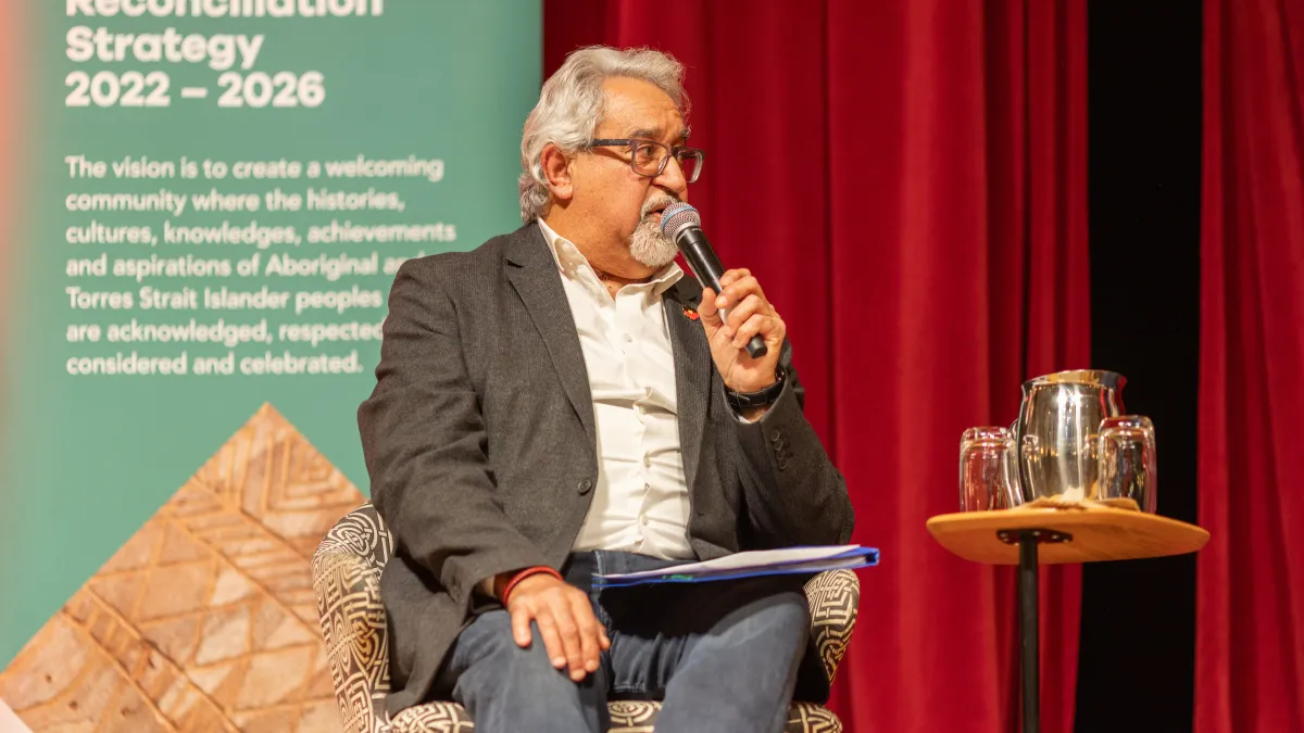 A man sits on stage holding a microphone.