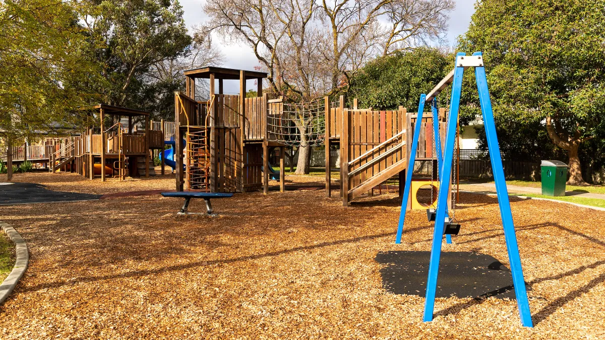 A wooden playground with a mulch floor including a swing set
