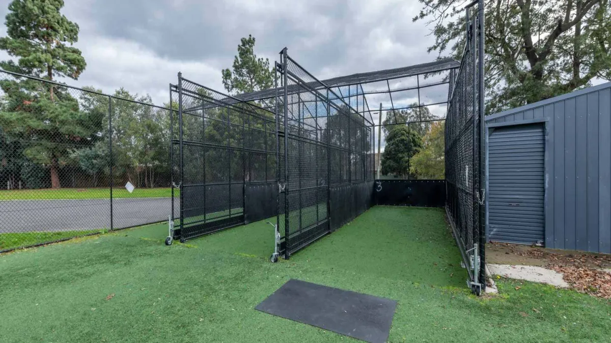 2 cricket nets with synthetic turf next to a small corrugated shed with a door