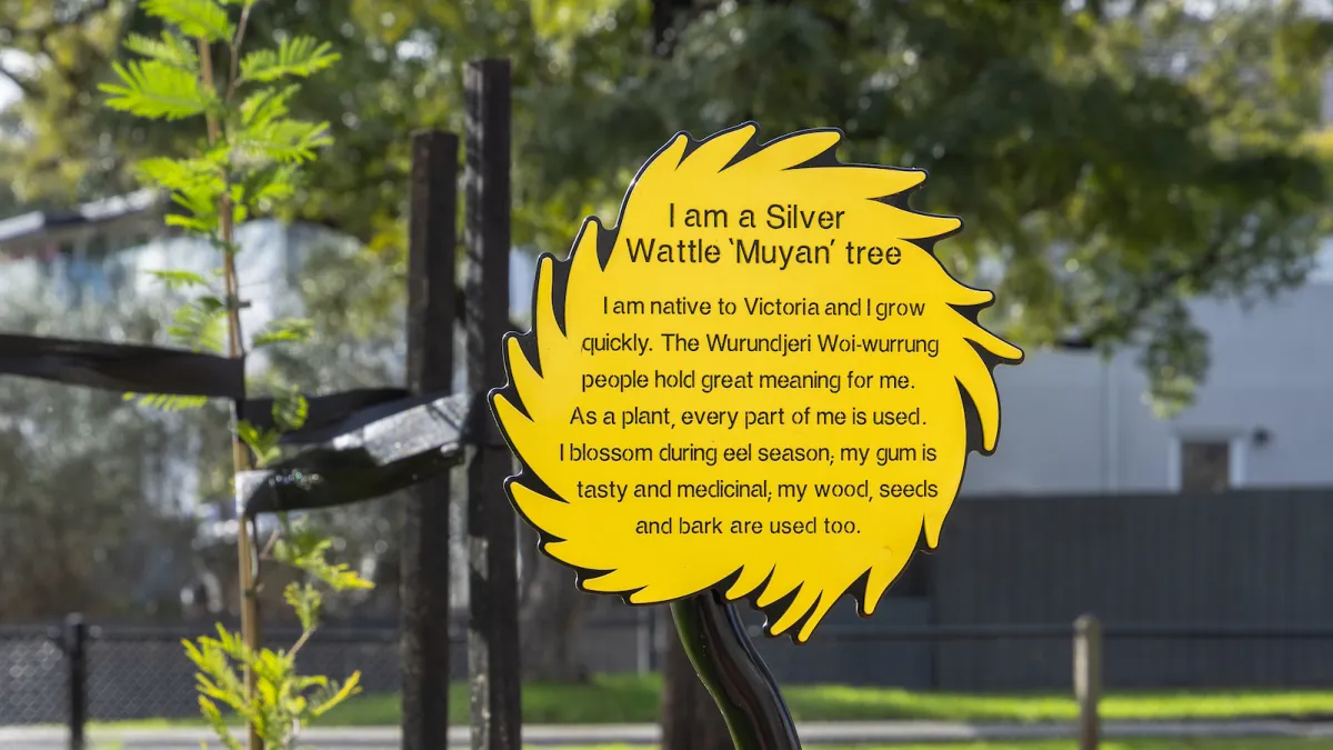 A wooden sculpture of a bird and a yellow sign with details about a tree