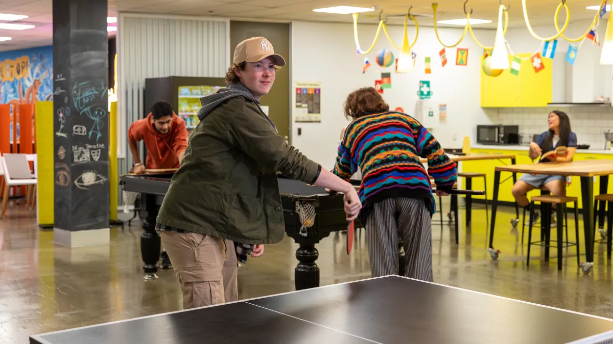 Young people play table tennis inside.