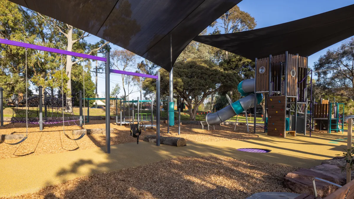 Two swing sets under shade cloth at a sunny playground
