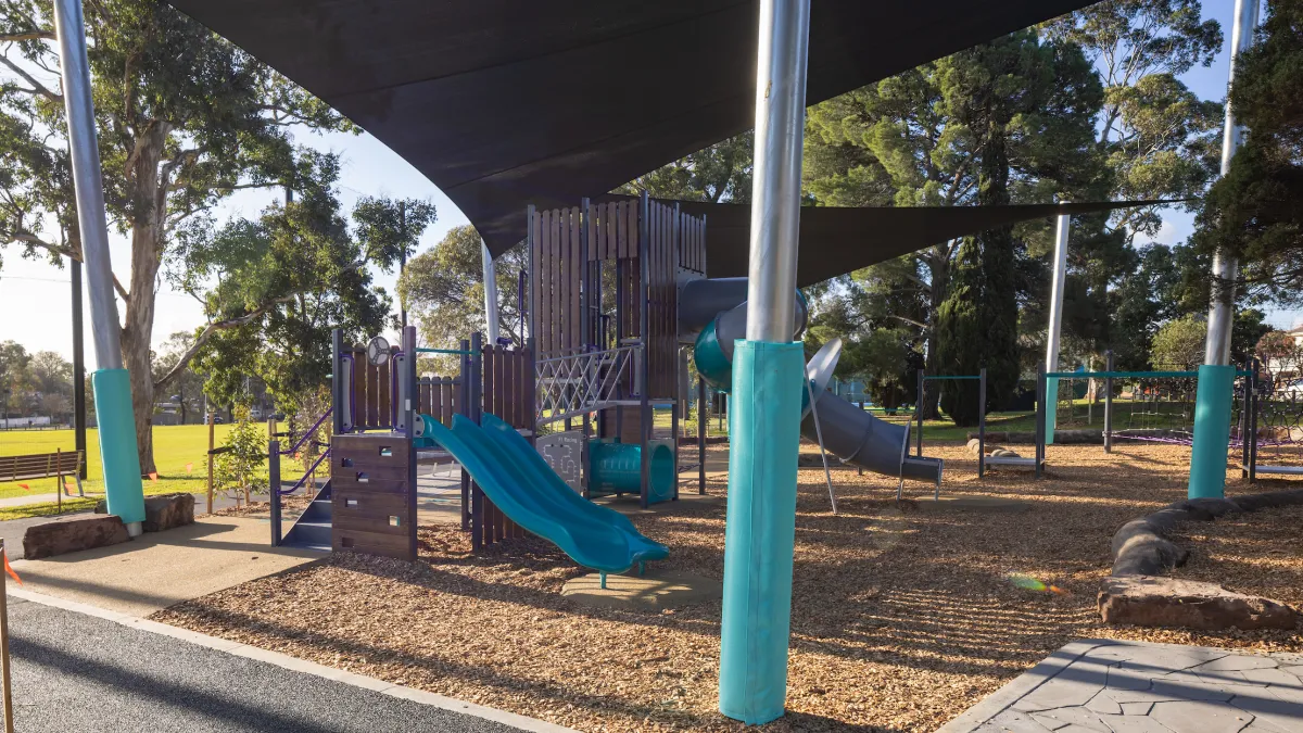 A large, black sail cloth shades a slippery dip in a playground