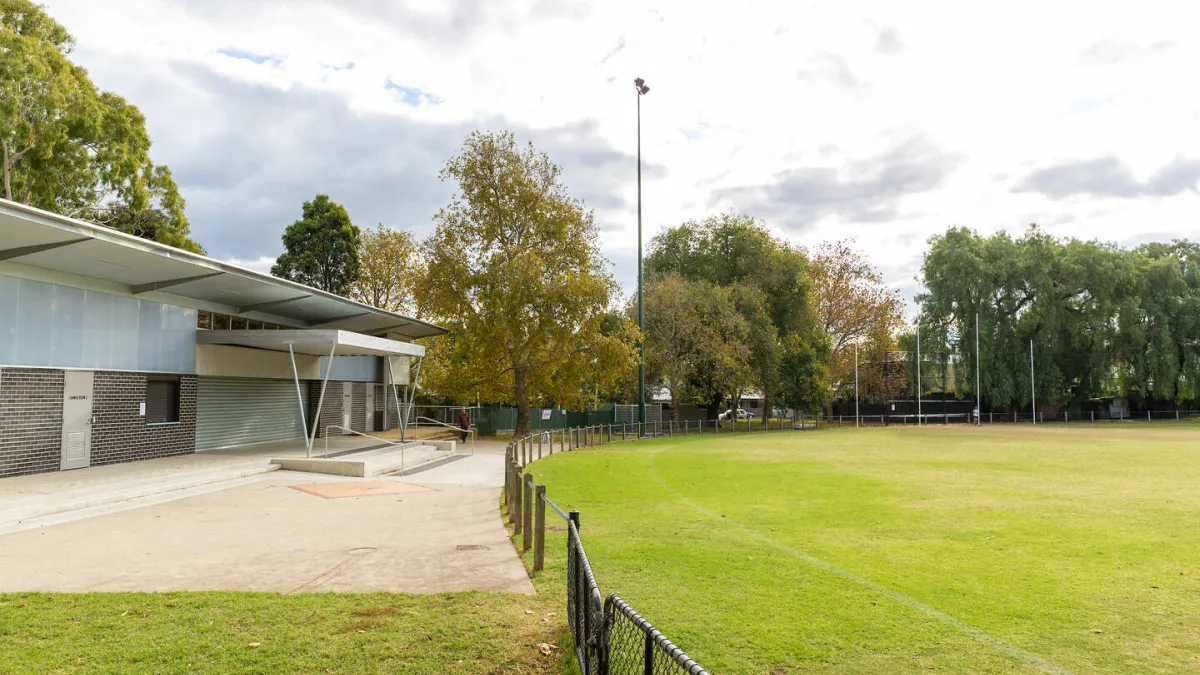 A AFL field, surrounded by a fence. A building with a sheltered area is to the left. 