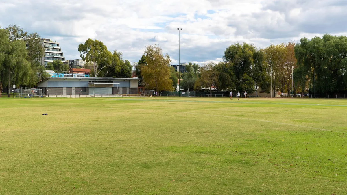 A green sports field with trees, goalposts and a buiding in the background. 