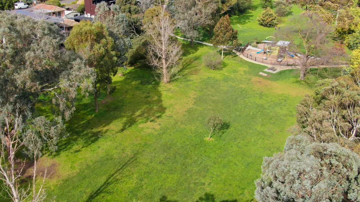 A park with a large open grass area and a playground surrounded by trees. 