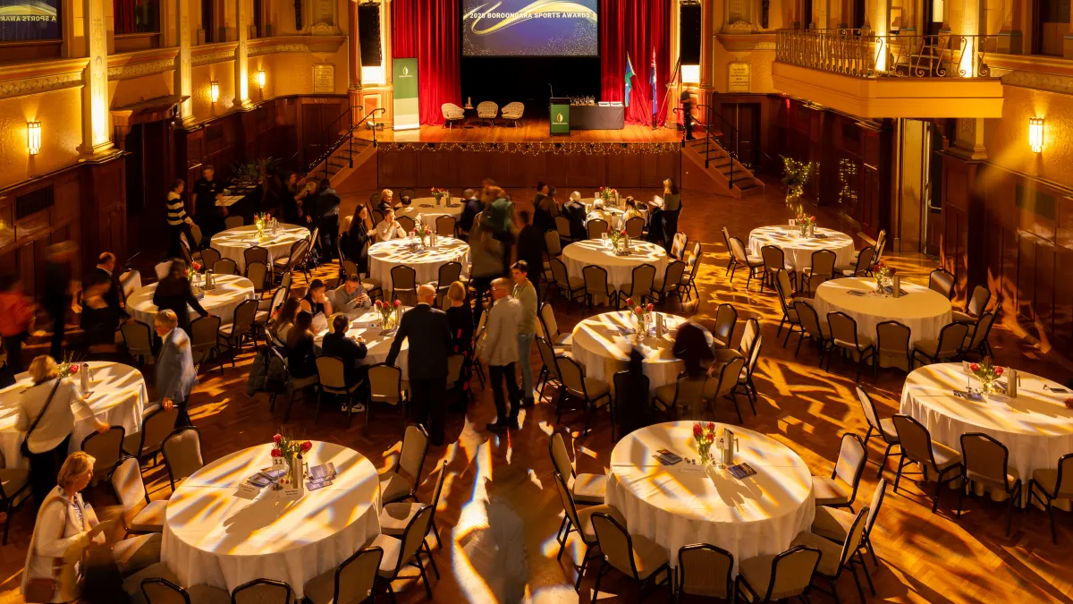 Banquet tables fill a fancy room with a stage in the foreground