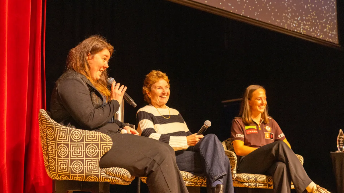 Three women with microphones look happy while sitting on a stage