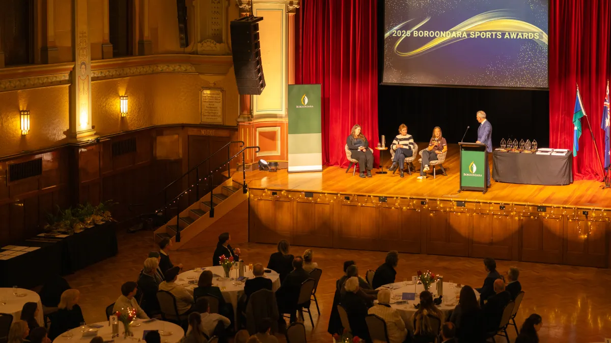 Four adults on a stage in front of a room full of banquet tables where an audience is seated