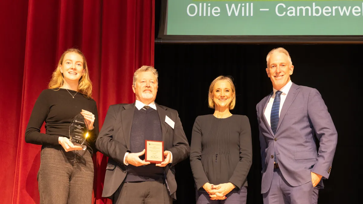 In front of a velvet curtain, 2 adults hold trophies and 2 other adults smile