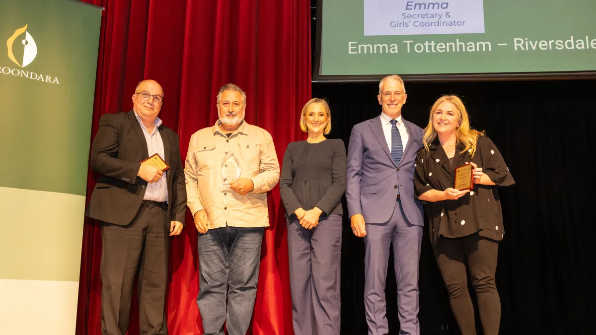 5 people stand on a stage, 2 of them are holding plaques