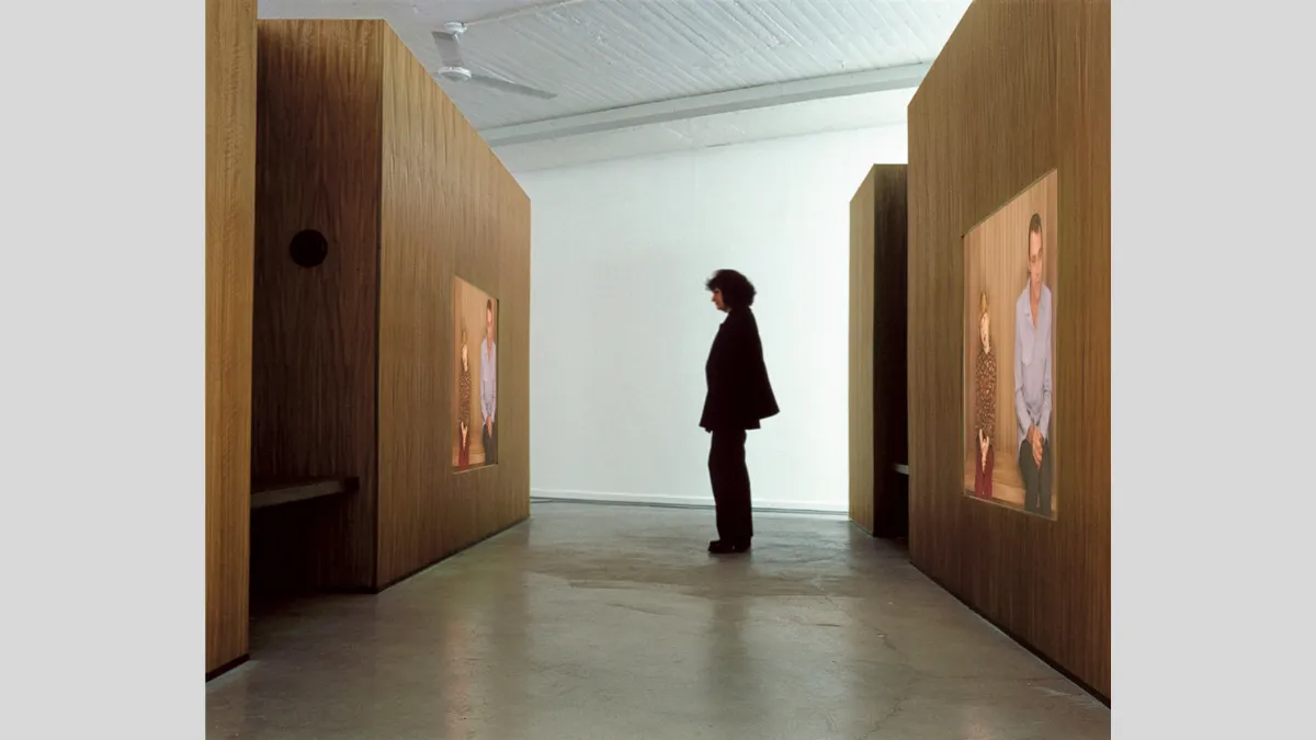 A person stands within a lobby-like structure with two videos projected onto the wood veneer