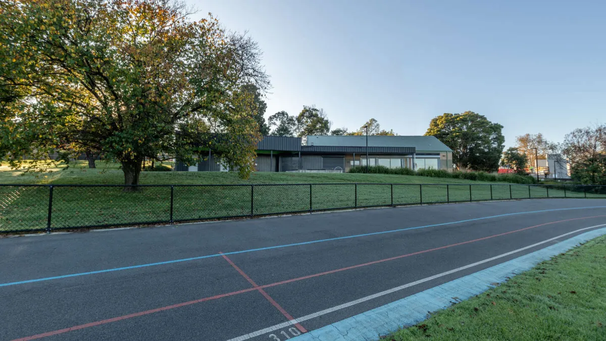 A segment of a cycling/running track surrounded by a short wire fence. in the background is a building and trees. 