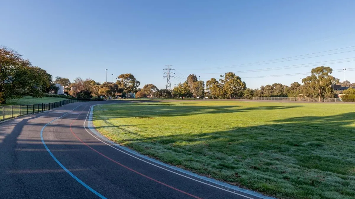 A curved segment of a cycling track with line markings. There is grass to either side and trees in the background. 