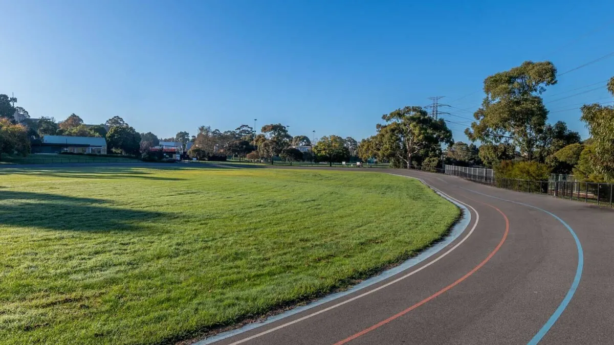 A segment of a cycling/ running track with red and blue line marking. There is grass next to the track. 