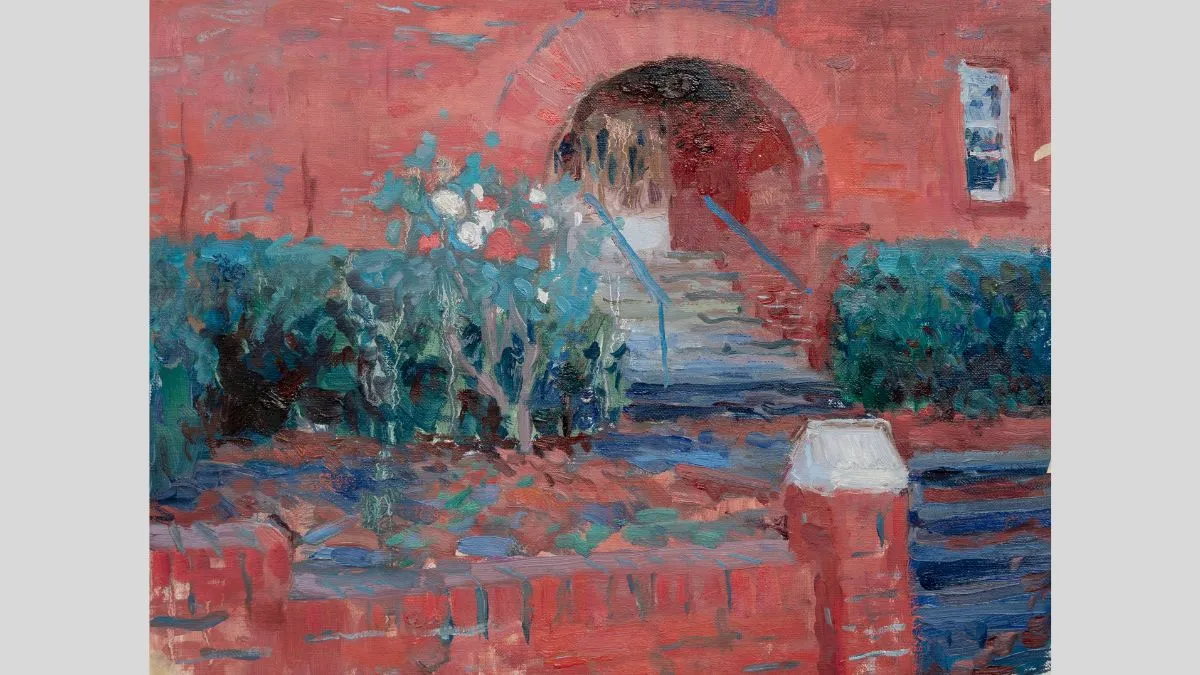 Façade of a building with red bricks. There are steps leading up to the arched doorway. Building is lined with green bushes. 