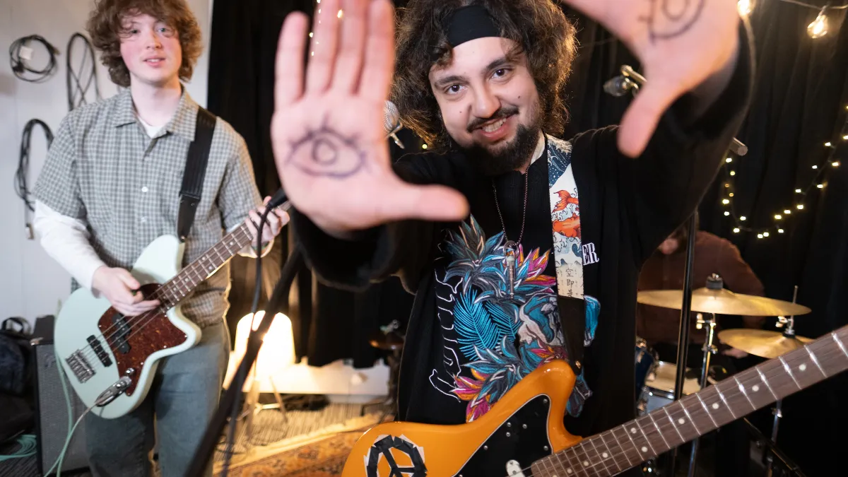 2 men with guitars, one with open eyes drawn on his palms in texta