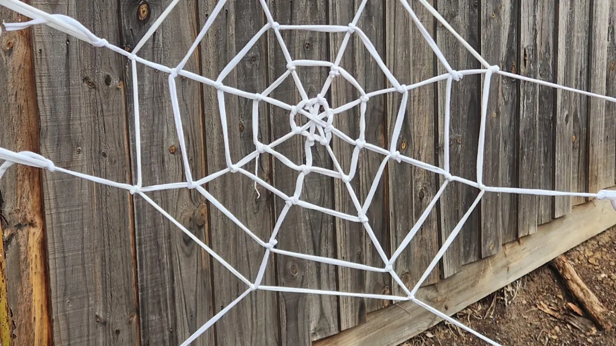 A fabric spider web against a wooden fence.