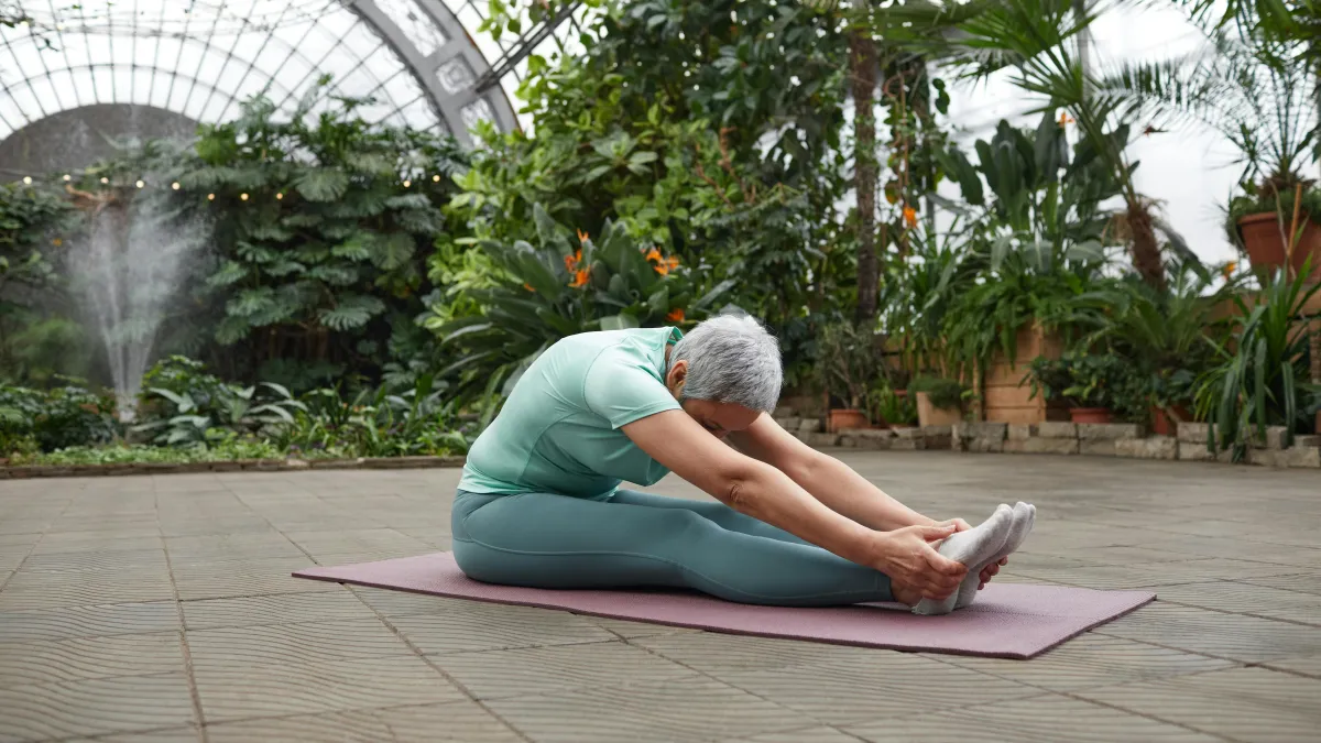 A woman has her legs out straight and is leaning forward to touch her toes.
