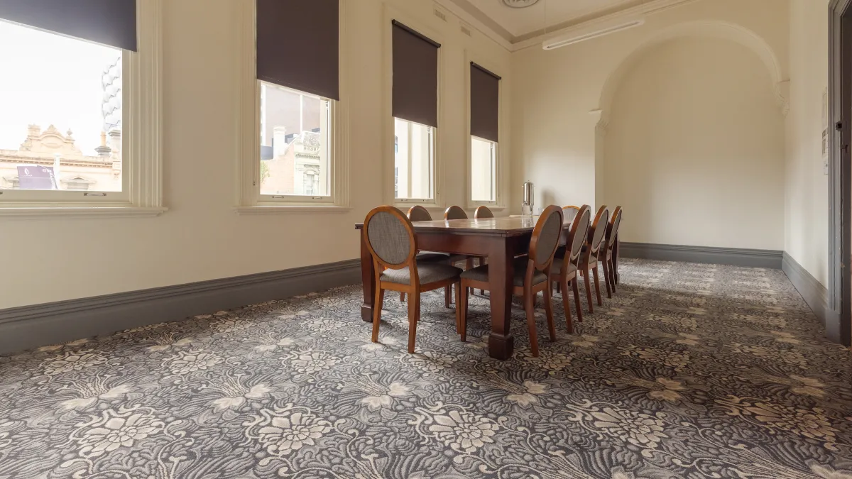 A conference room showing a large meeting table with chairs, windows, and patterned flooring.