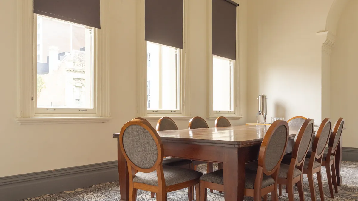A Meeting room featuring a long wooden table, 8 chairs, three windows with shades, and patterned carpet.