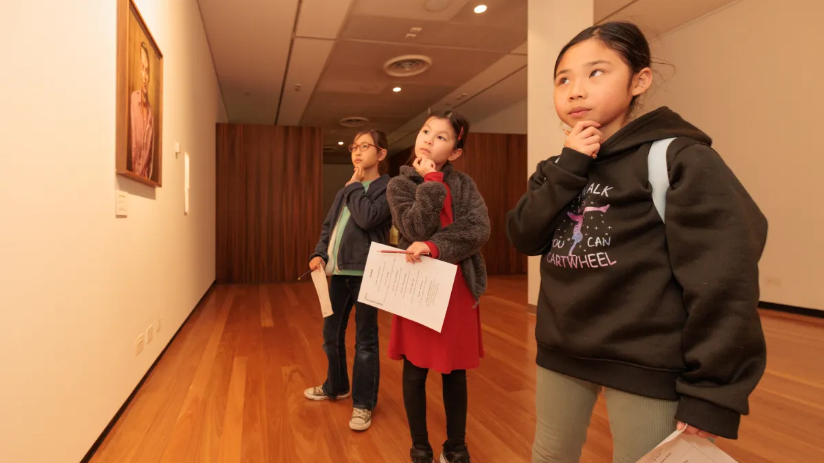 Three young people looking thoughtfully at artworks in a gallery. 