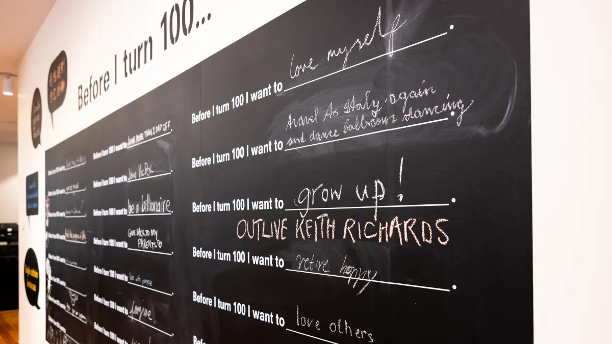 A blackboard with writing on it that finishes the sentence "Before I turn 100 ..."