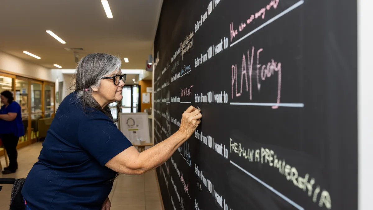 An older person writes on a blackboard