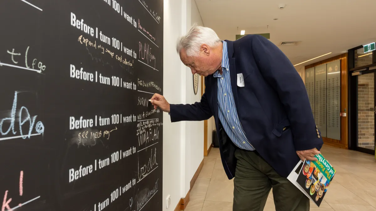 A senior citizen writes on a blackboard