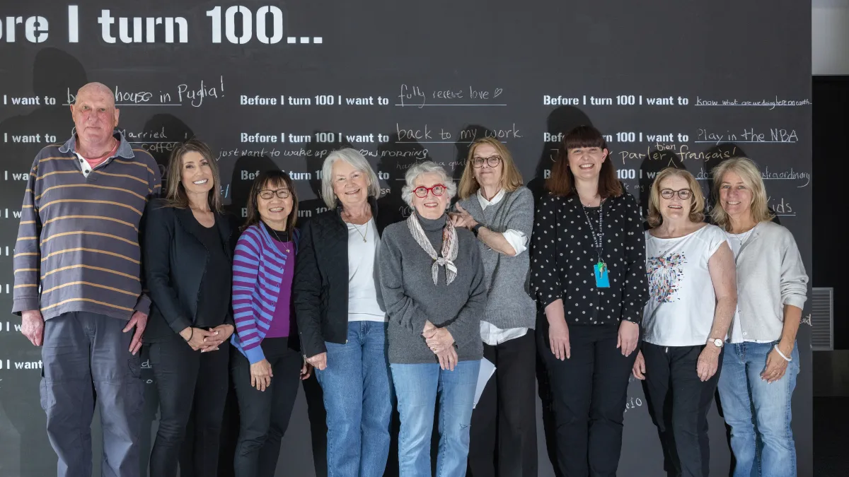 A group of men and women stand in front of a blackboard with writing on it