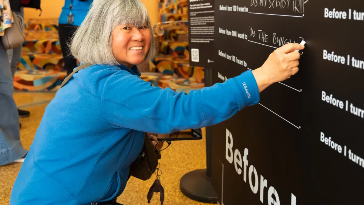 A woman kneels and writes with chalk on a board