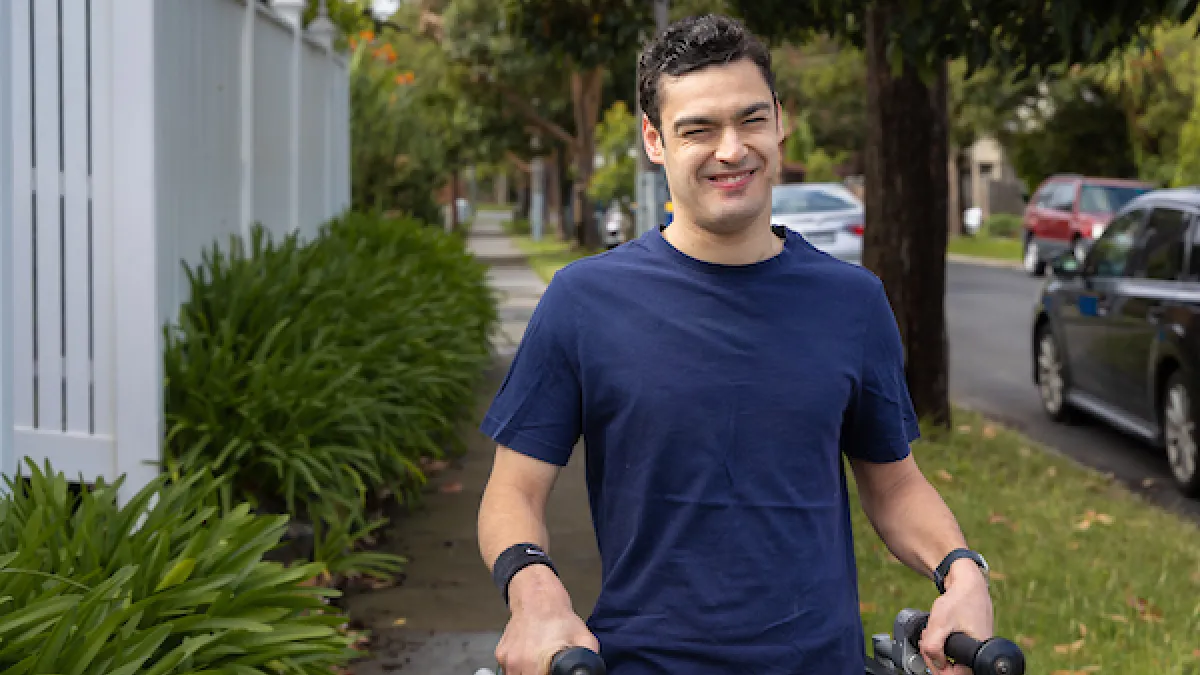A young man standing outstide with crutches smiling at the camera