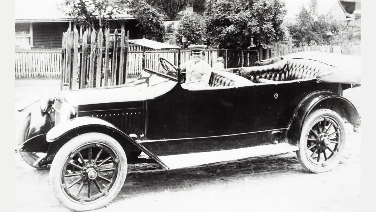 A woman at the wheel of a classic, open-top vintage car