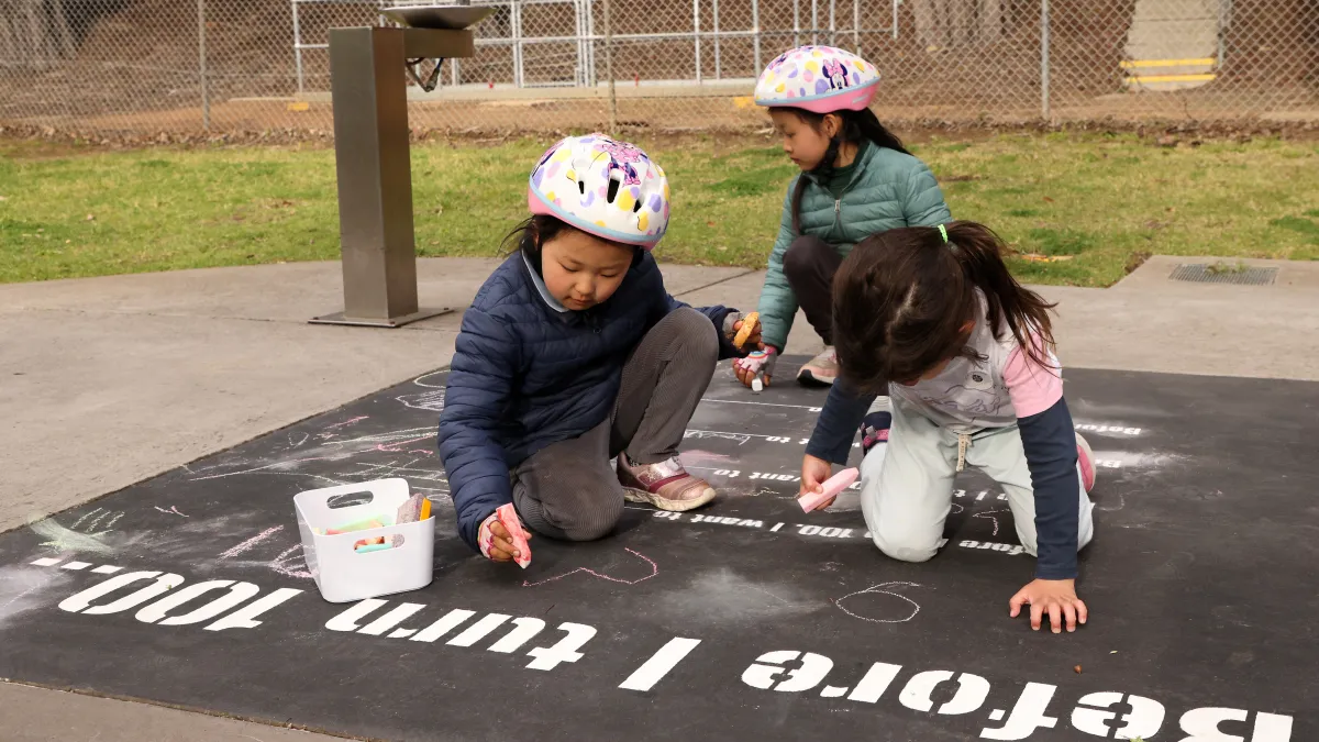 Two children in bike helmets write in response to a written prompt, 'Before I turn 100 ...'