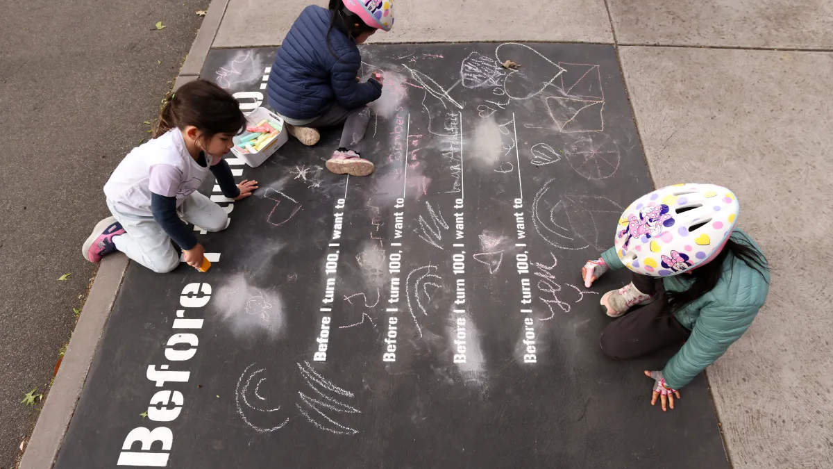 Three kids in bike helmets write in response to a prompt, 'Before I turn 100 ...'