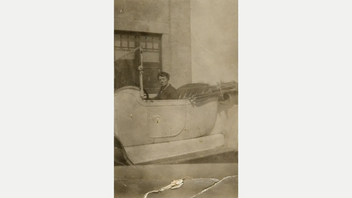 Faded sepia photo of a woman in a large, open-top car