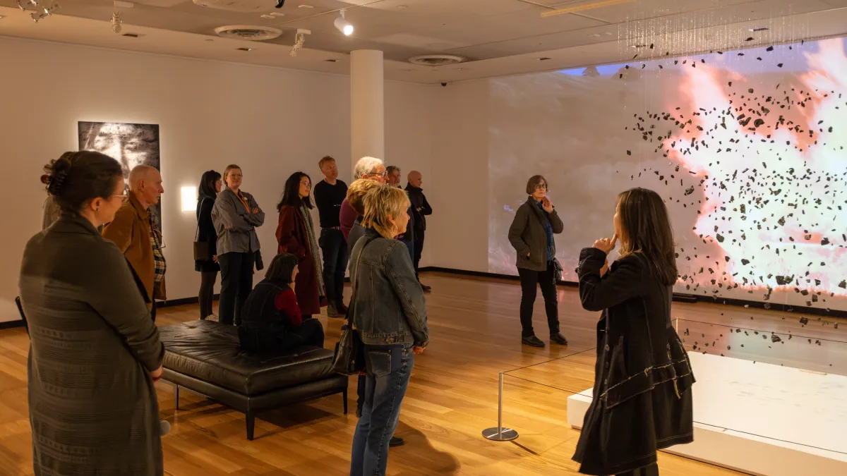Visitors listening to artist Cyrus Tang speak about her artworks on display including a video of fire and a suspended sculpture of tiny pieces of a burnt piano. 