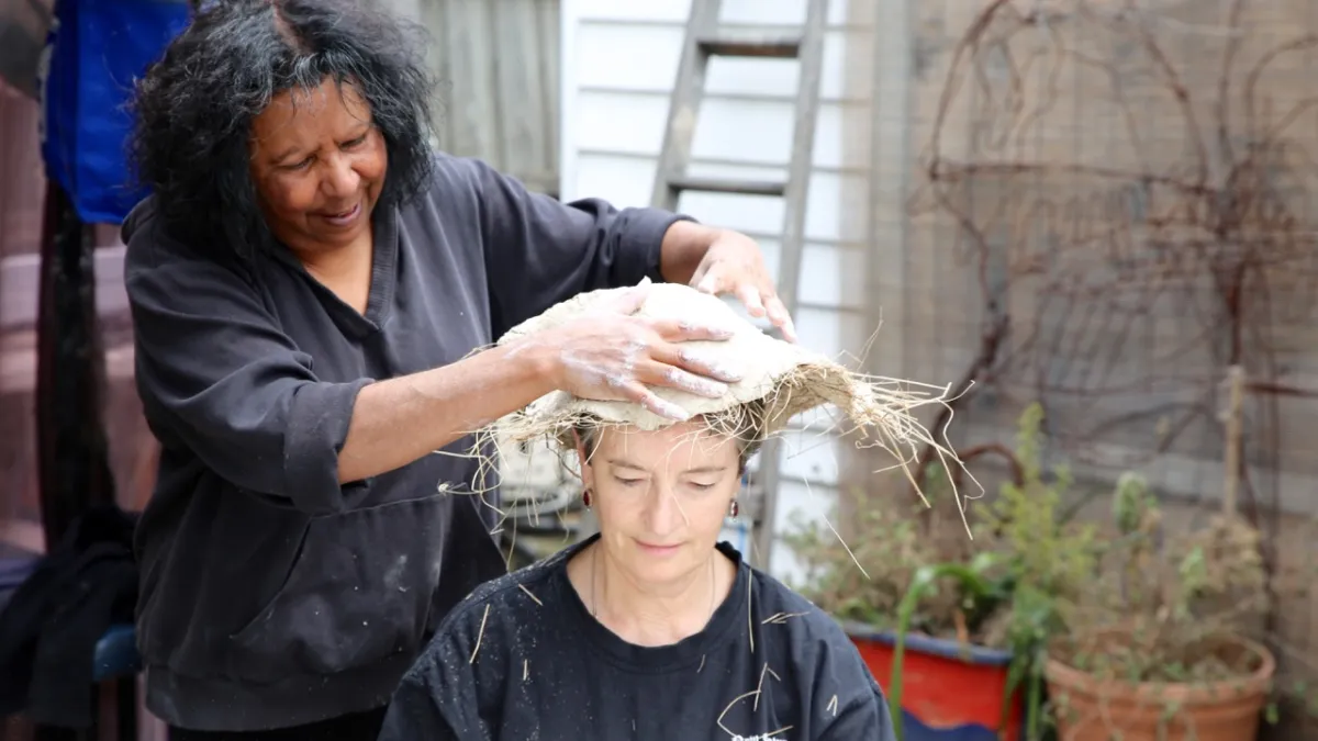 A woman places an Indigenous Australian mourning cap, kopi, on the head of another woman.