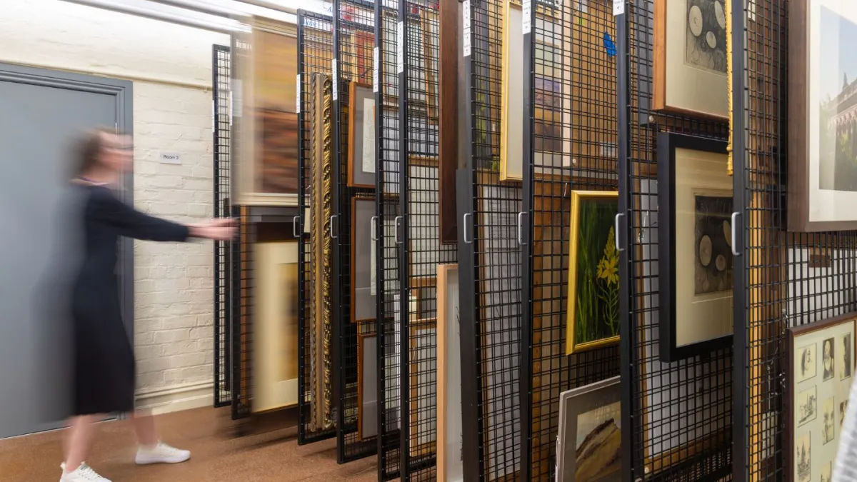 A photograph of blurry figure pulling out a rack of artworks