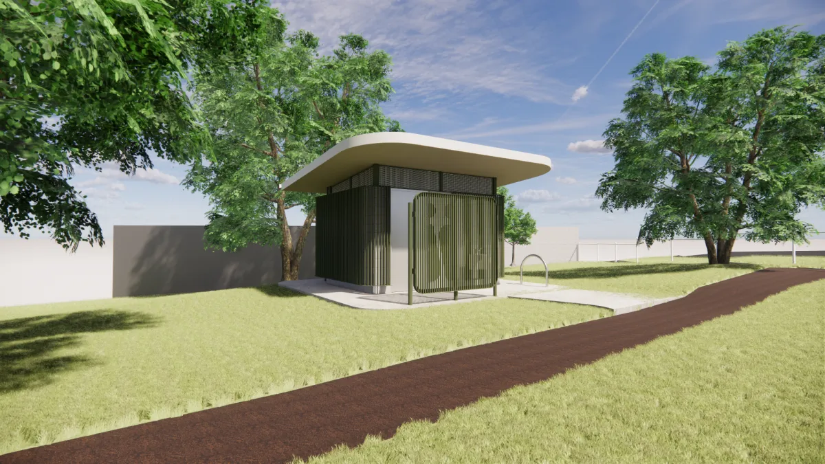 Side view from the east of a green and cream toilet block. It joins onto a brown path and has medium to large sized trees around it.