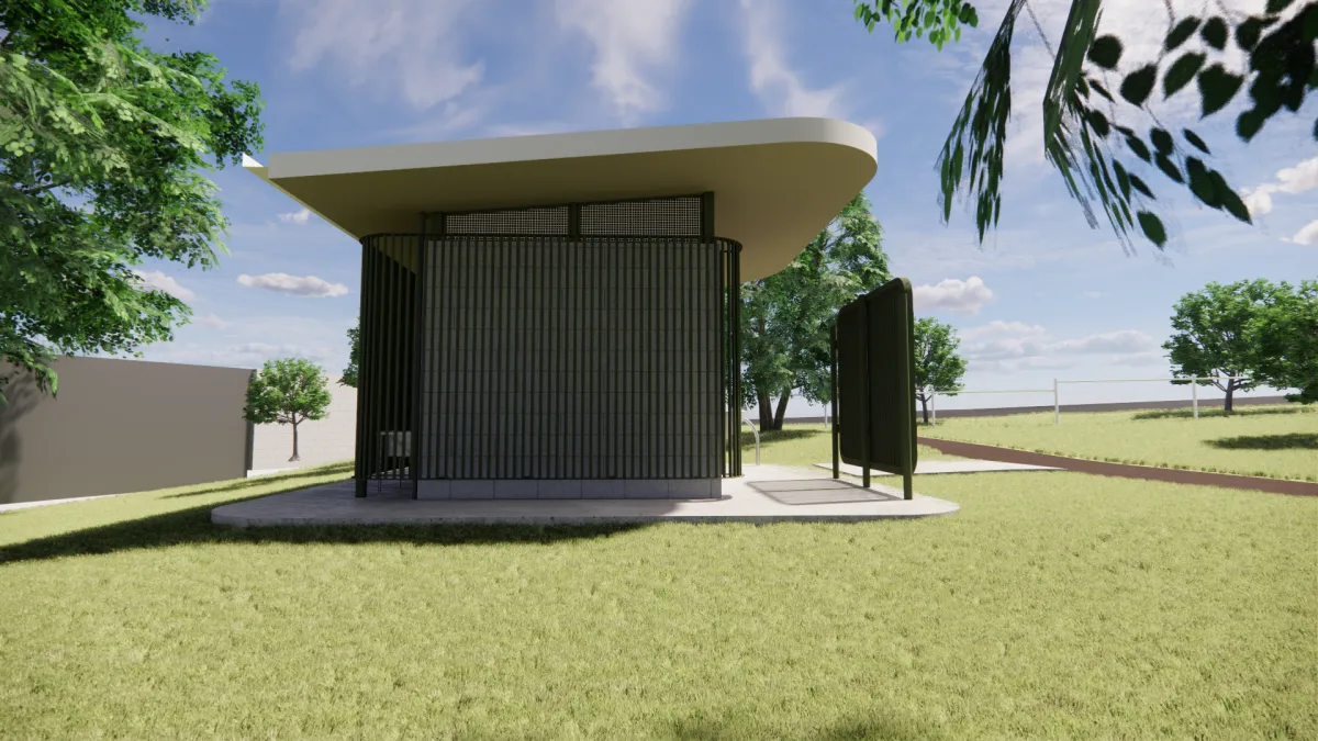 The rear of a green and cream toilet block. It joins onto a brown path and has medium to large sized trees around it.