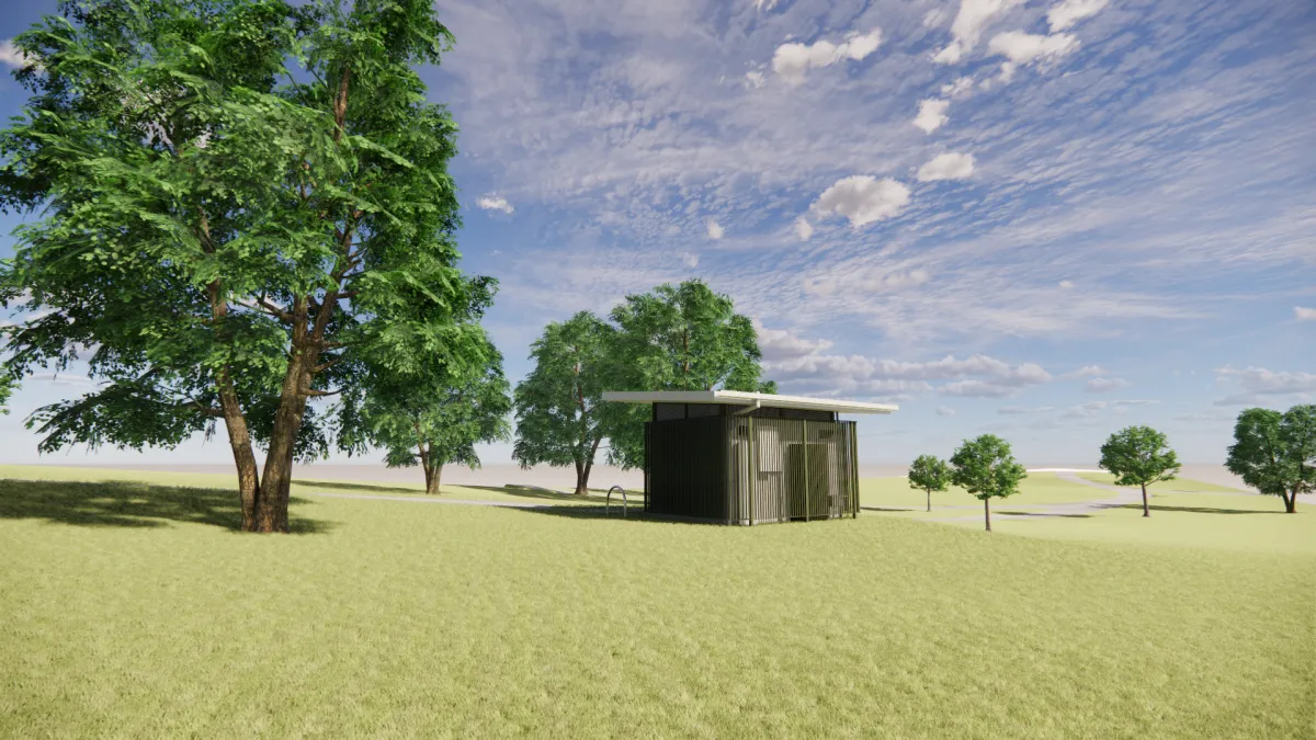 Side view from the West of a toilet block. It is next to a footpath and surrounded by trees. The toilet is green and cream to help it blend into the surroundings.