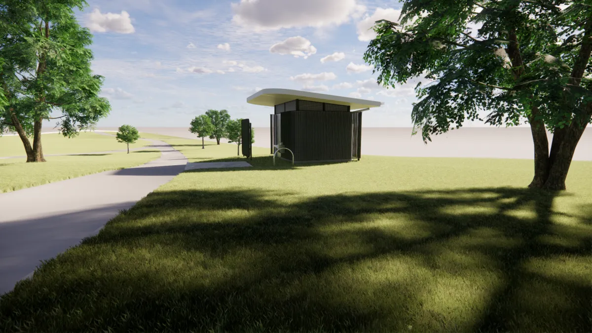 Side view from the west of a toilet block. It is next to a footpath and surrounded by trees. the toilet is green and cream to help it blend into the surroundings.