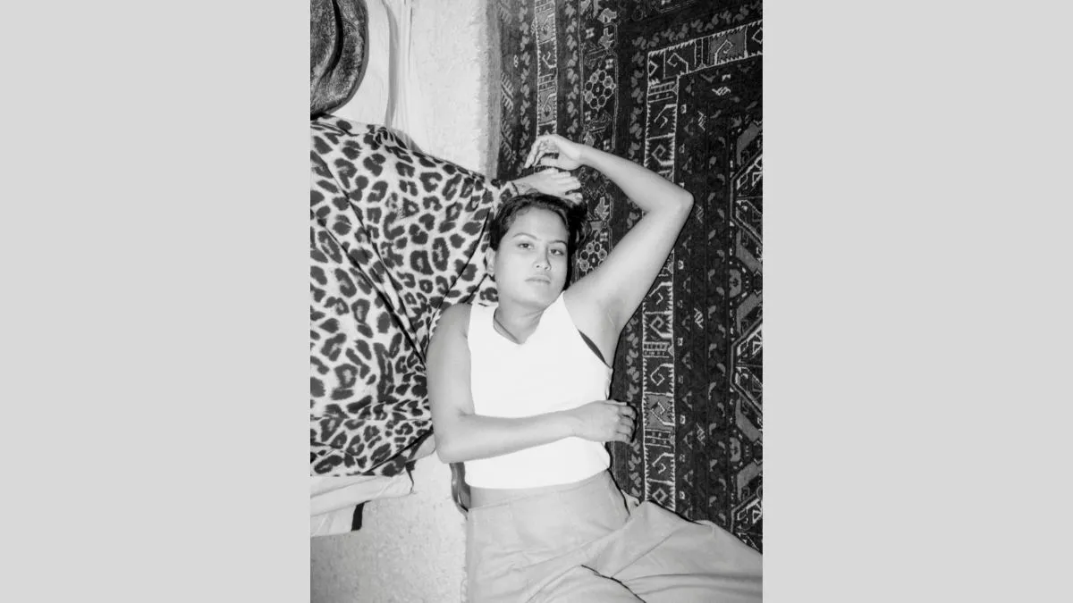 A black and white image of a person lying on a rug, their head rests on another persons feet and left arm reaches above their headd. 