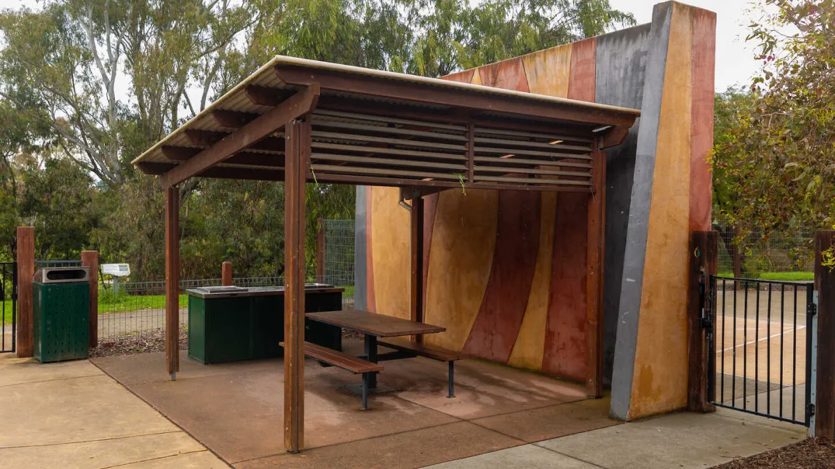 A picnic shelter including a picnic table, barbecue and bin undercover. 