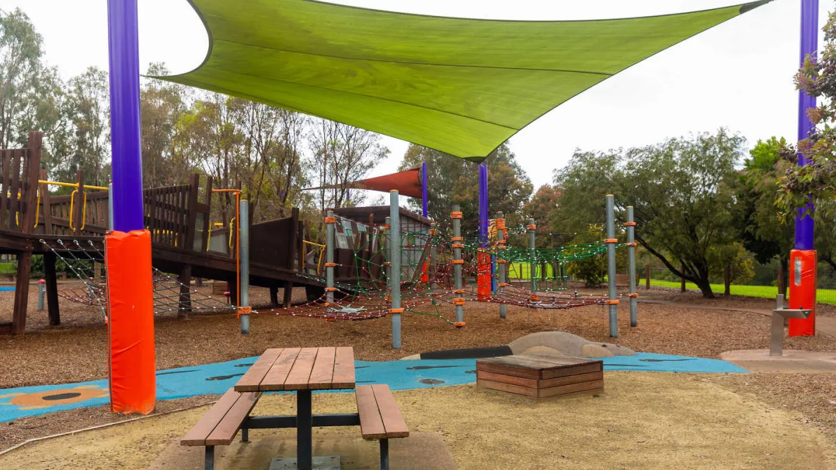 A playground under a shade sail, and a picnic table